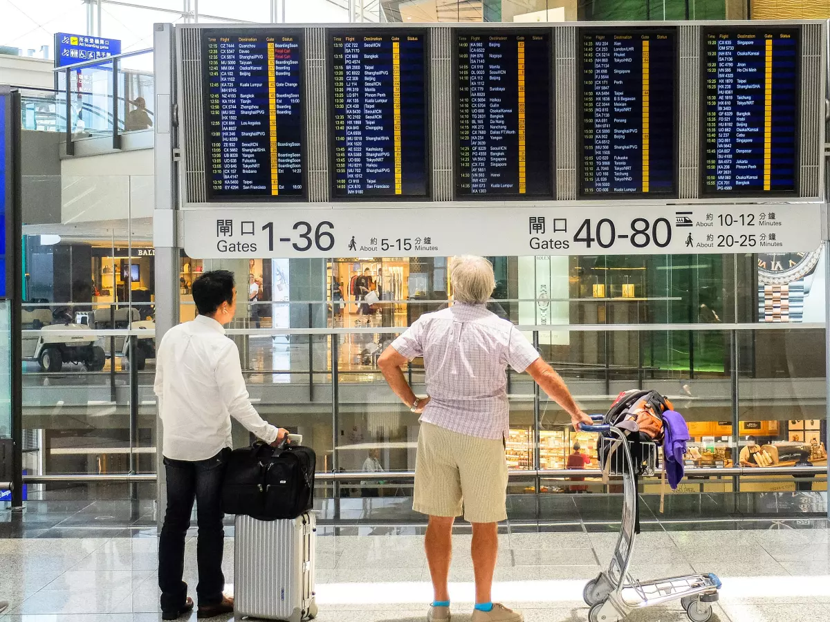 Two people stand in front of a large flight information board, looking at the schedule.