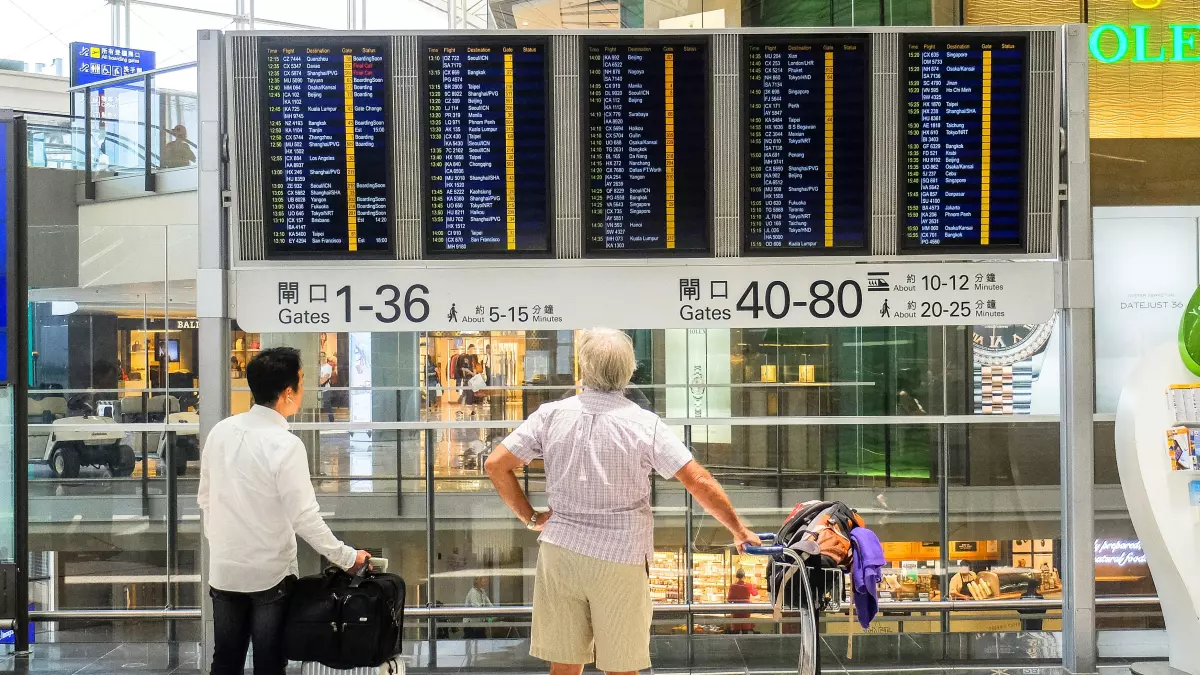 Two people stand in front of a large flight information board, looking at the schedule.