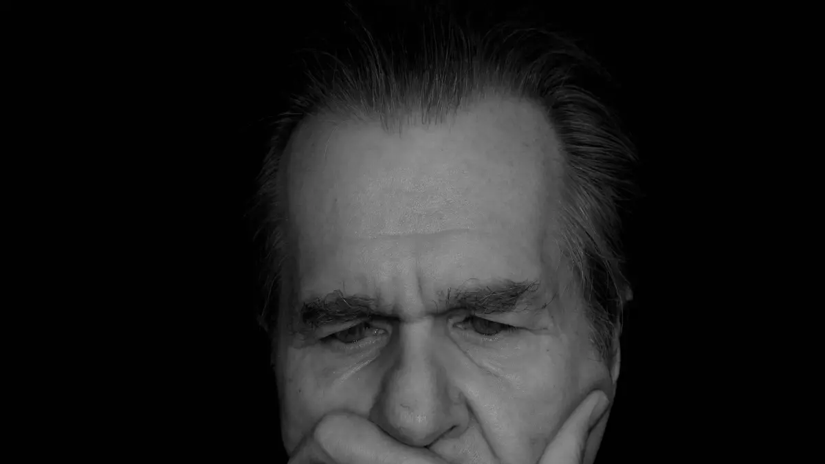 A man with grey hair is thinking deeply. He is looking down and has his hand on his chin.