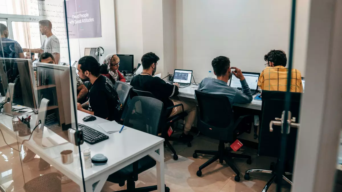 A group of people working on computers in a modern office with glass walls.