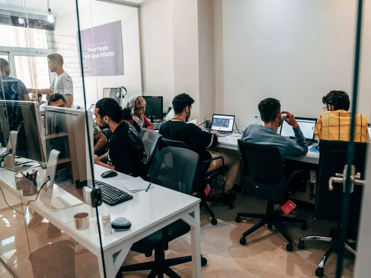 A group of people working on computers in a modern office with glass walls.