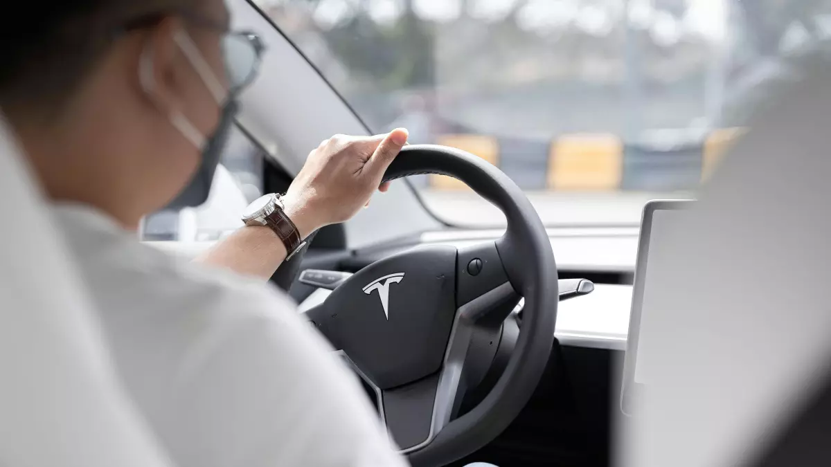 A person driving a Tesla car with a steering wheel in their hands