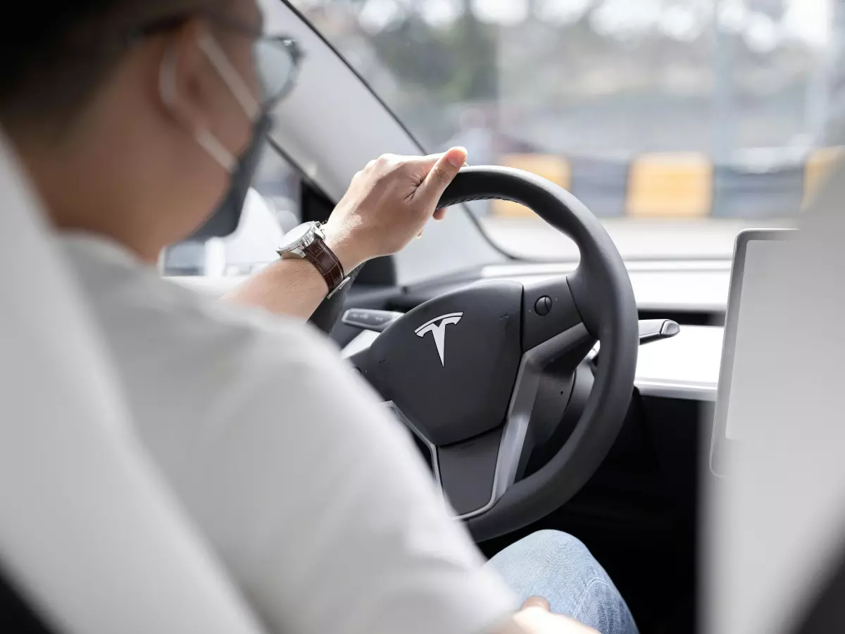 A person driving a Tesla car with a steering wheel in their hands