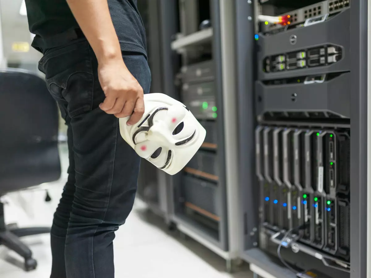 A person holding a Guy Fawkes mask in front of a server rack.