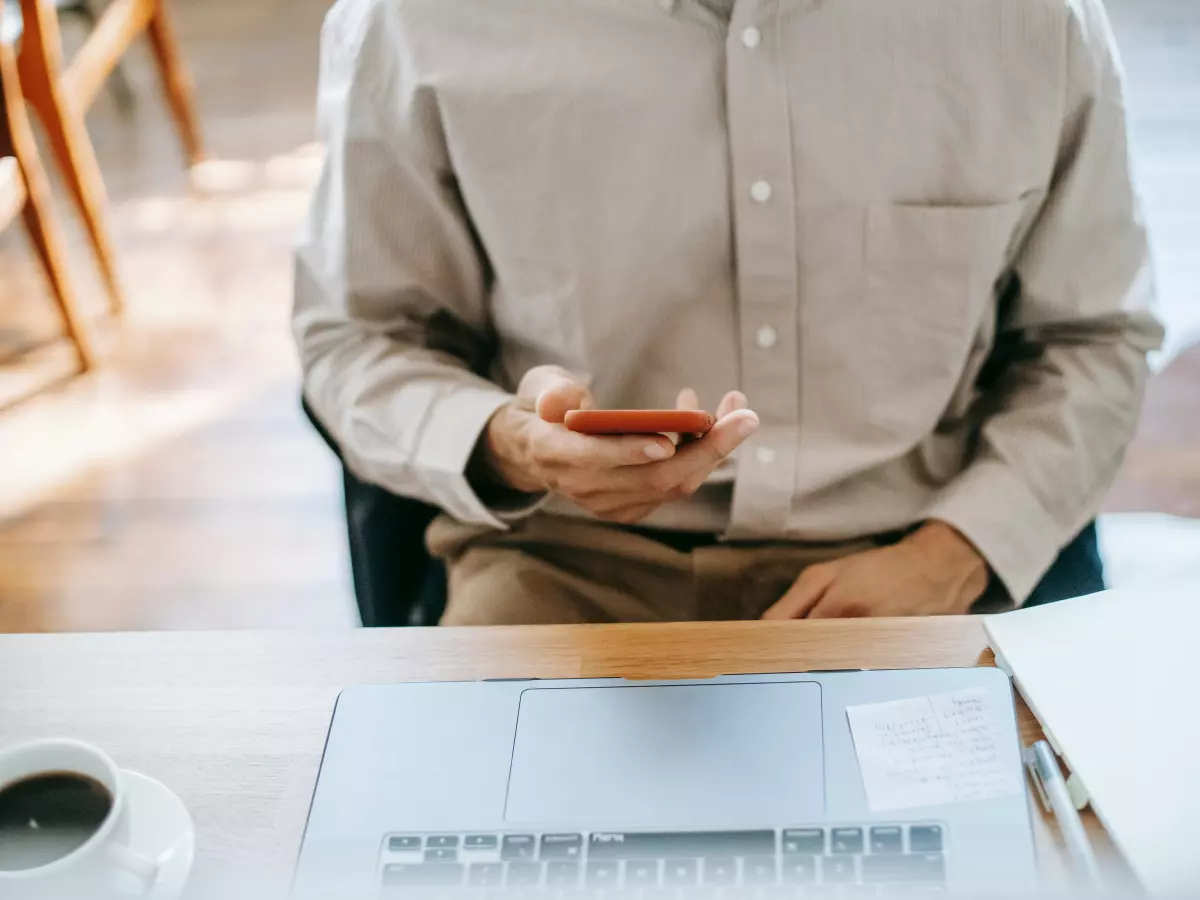 A person in a beige shirt sitting at a desk and using a smartphone.