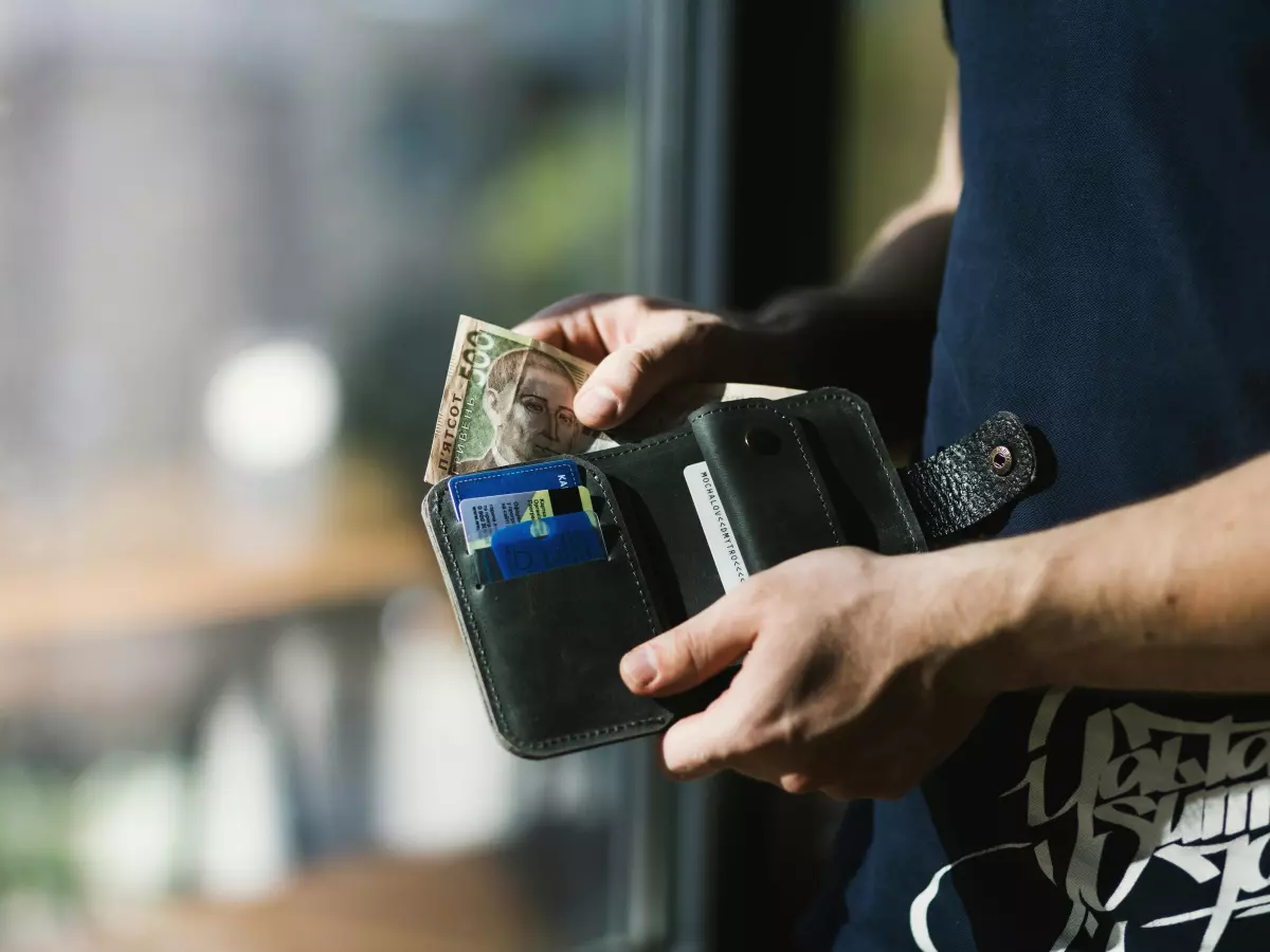 Close-up of a hand reaching into a wallet, holding cash and cards.