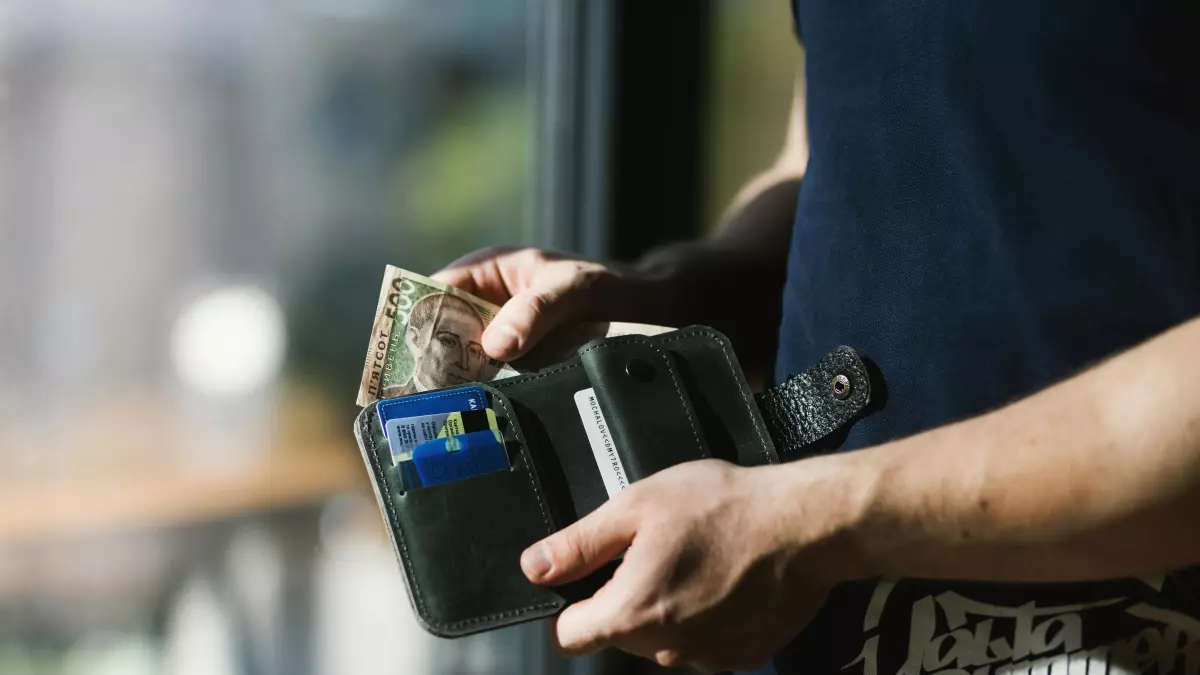 Close-up of a hand reaching into a wallet, holding cash and cards.