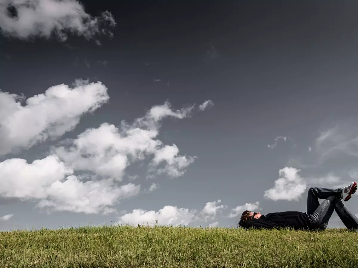 A person lying on their back in a field of grass, looking up at the sky.