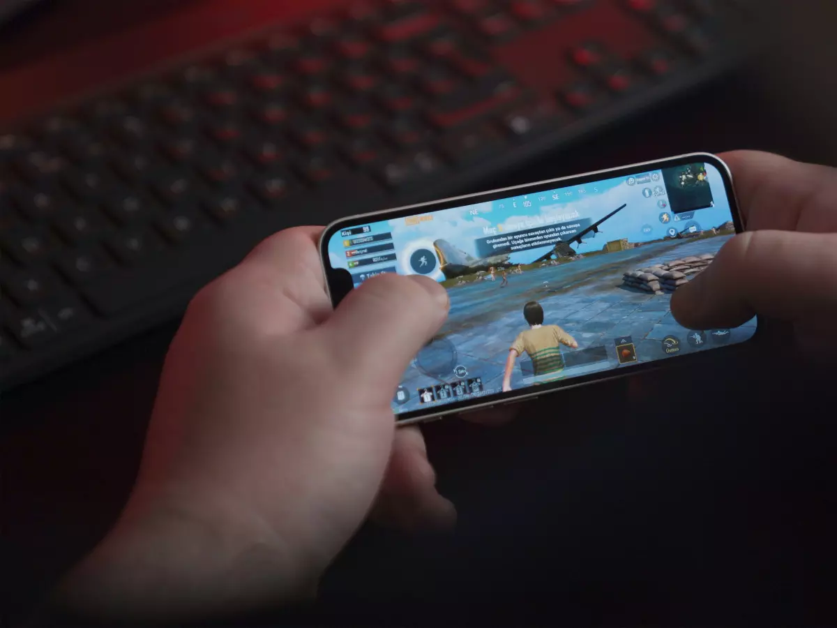 A person's hands holding an iPhone, playing a game on it, with a keyboard in the background.