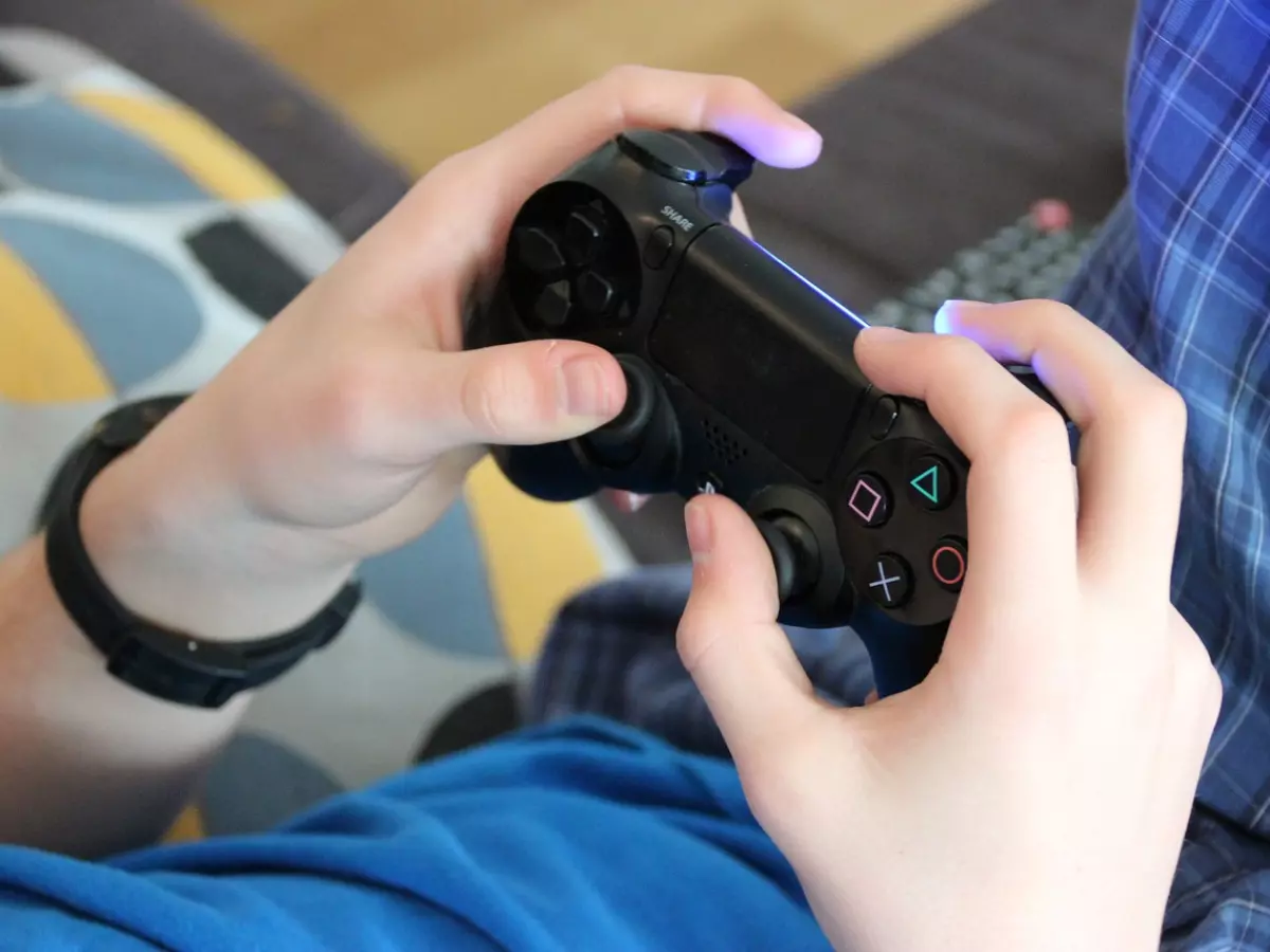 Close-up of hands holding a video game controller, with a blue shirt and a black wristwatch in the background.