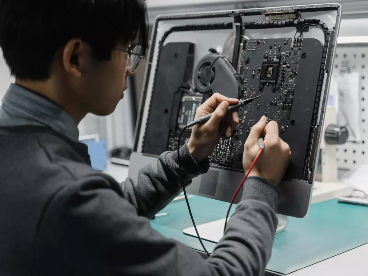 A person in a black shirt is using a soldering iron to fix a circuit board, with the back of their hand resting on the board.