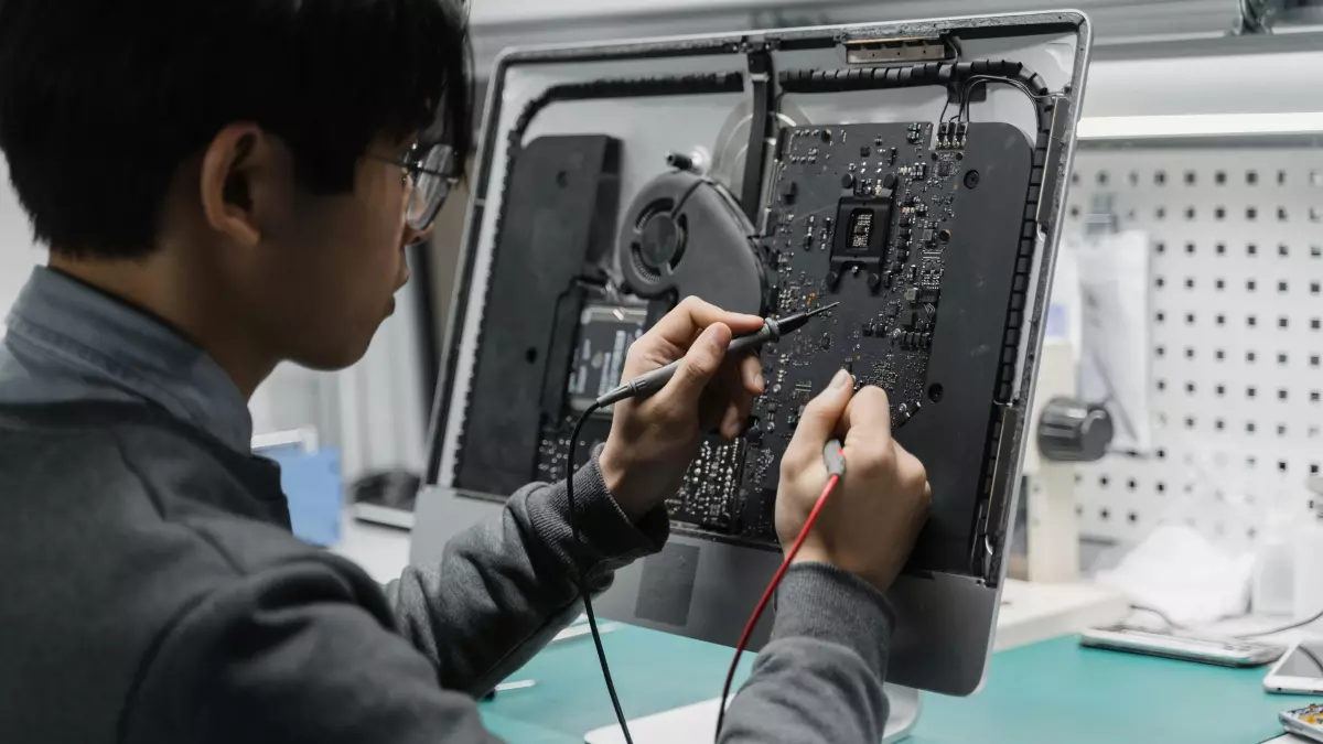 A person in a black shirt is using a soldering iron to fix a circuit board, with the back of their hand resting on the board.