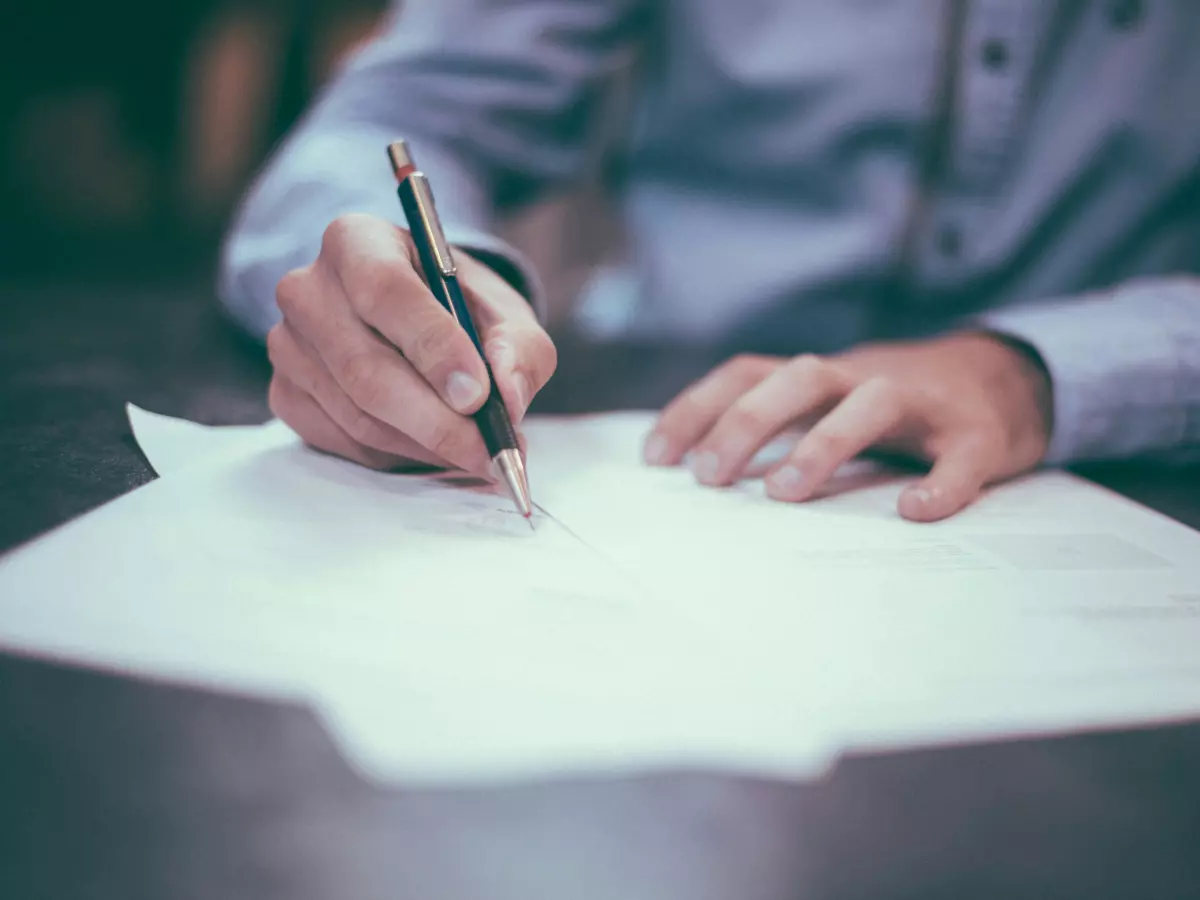 A close-up shot of a person's hand writing on a piece of paper with a pen.