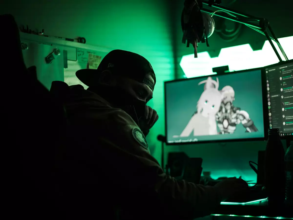 A gamer in a dark room, wearing a cap and a mask, sitting in front of a monitor with a game displayed.