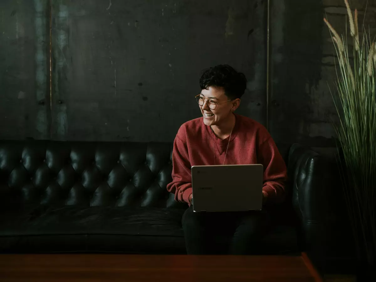 A young woman in a red shirt with a laptop, smiling.