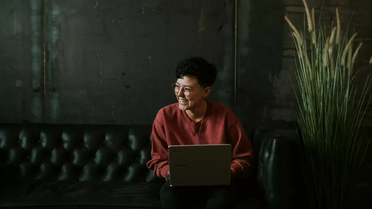 A young woman in a red shirt with a laptop, smiling.