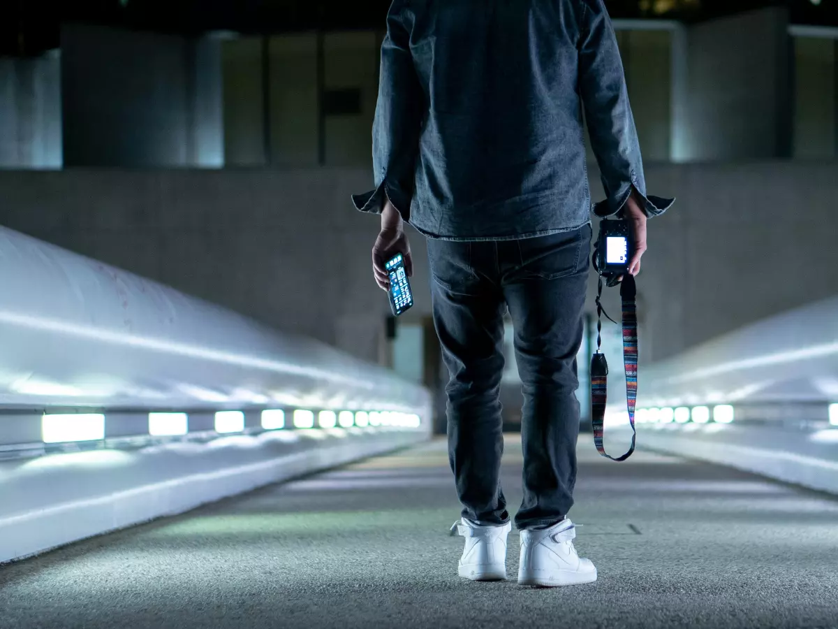 A person in a dark blue shirt and black pants walks away from the camera down a white, illuminated hallway.  The person is holding a smartphone in their right hand, which is obscured from view.