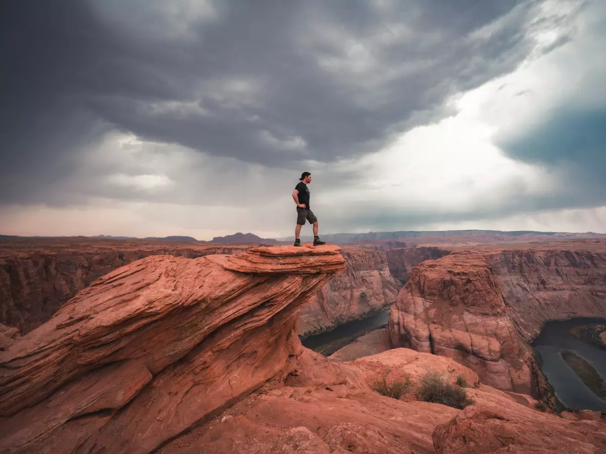 A man standing on a cliff with a storm cloud overhead