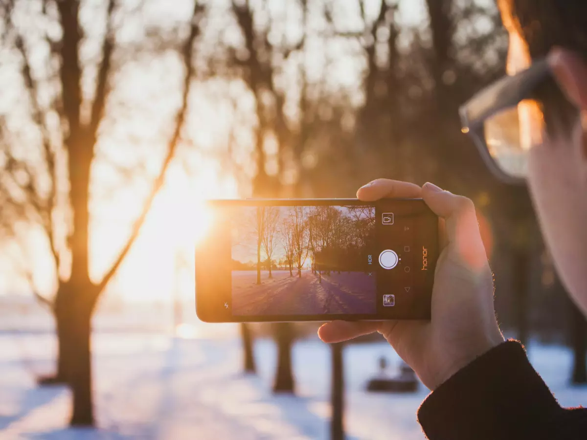 A person taking a photo with a smartphone in front of a sunset.