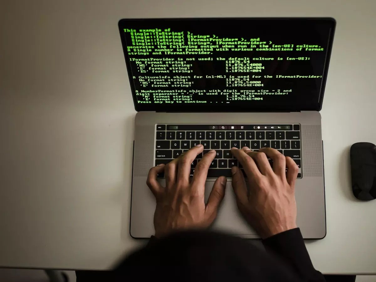 A person typing code on a computer. The screen is showing a lot of code. The person's hands are visible, but the person's face is not.