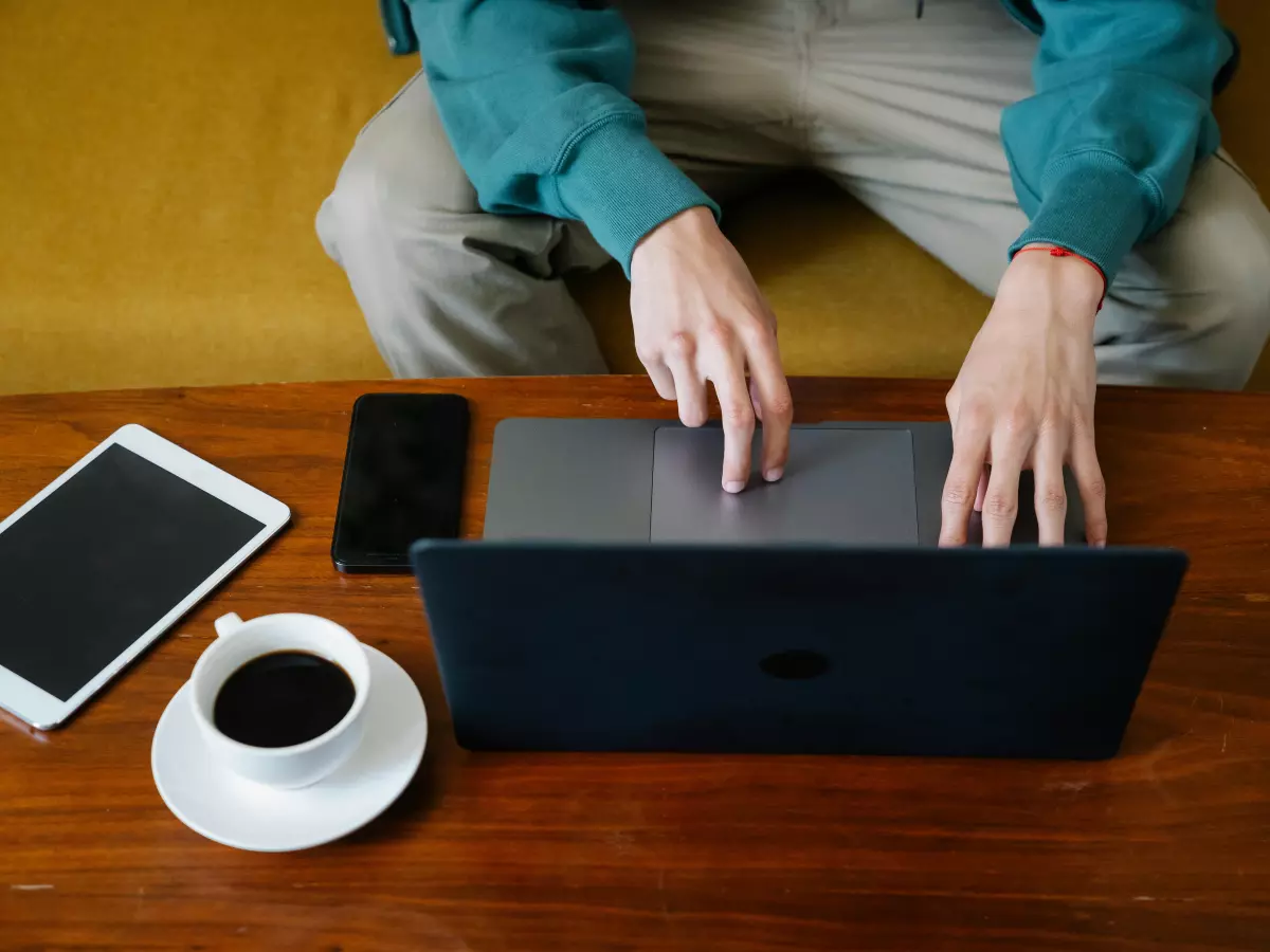 A person is working on a laptop, with a tablet, a smartphone and a coffee cup on the table next to them. 