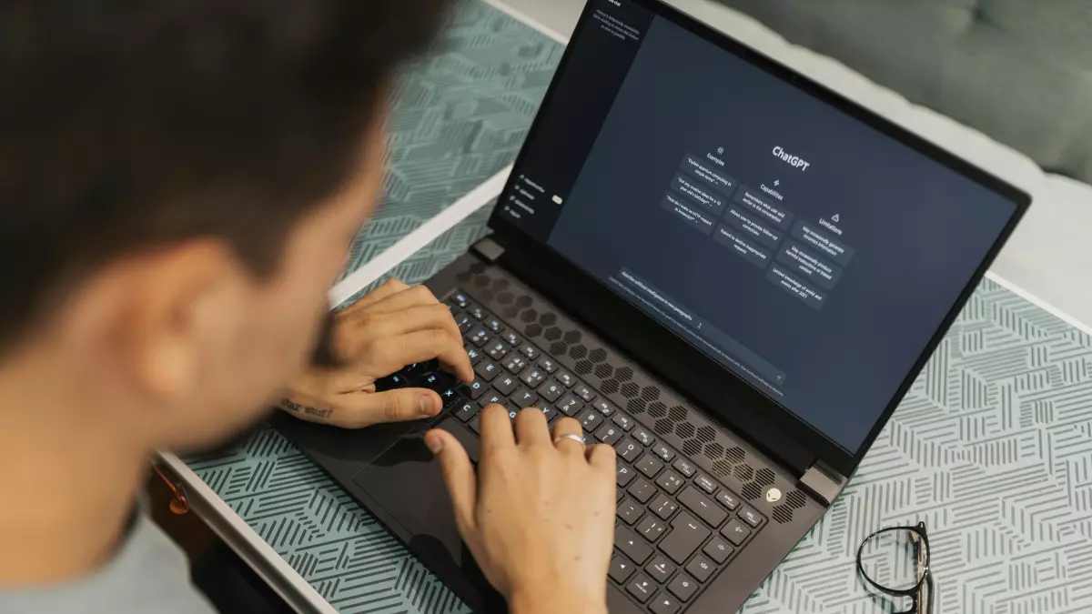 A person is using a laptop computer. The laptop is on a desk, and the person is typing on the keyboard. The image is shot from a low angle, and the person