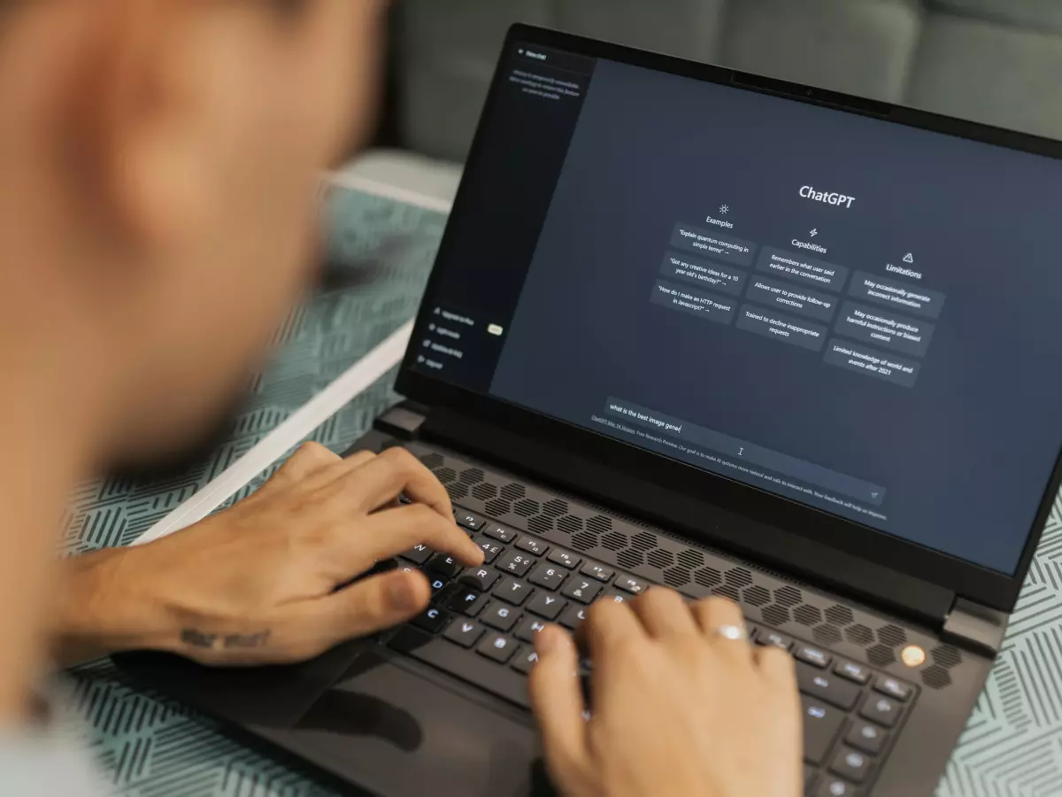 A person is working on a laptop computer. The person's hands are on the keyboard. The computer screen is displaying a dark background and code.