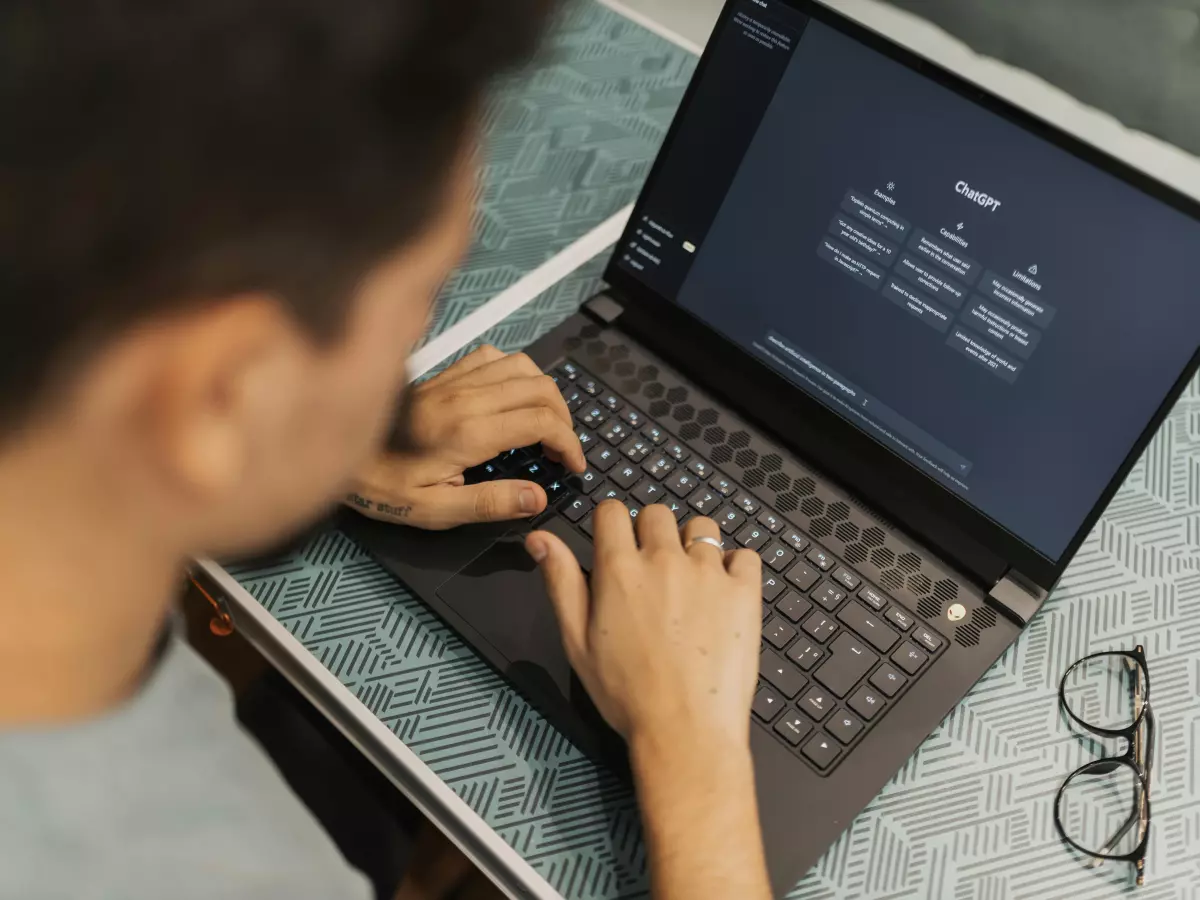 A person is using a laptop computer. The laptop is on a desk, and the person is typing on the keyboard. The image is shot from a low angle, and the person's face is not visible.