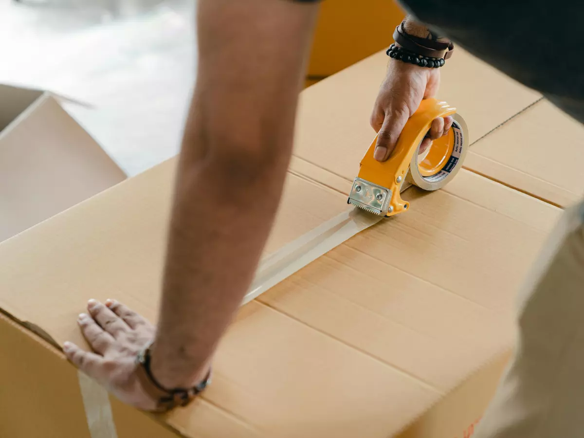 A person is using tape to seal a cardboard box.