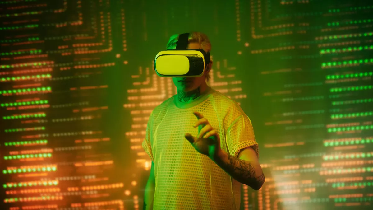 A young man with a VR headset on in front of a glowing green wall with lines and data patterns. He is reaching out with his right hand.