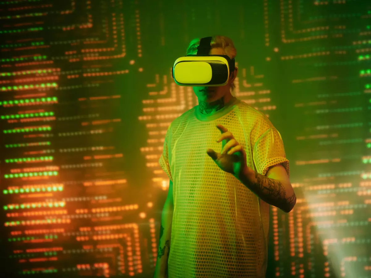 A young man with a VR headset on in front of a glowing green wall with lines and data patterns. He is reaching out with his right hand.