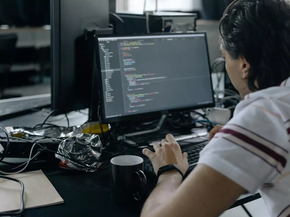 A person sitting at a desk, looking at a computer screen with code. The image suggests a serious and focused atmosphere