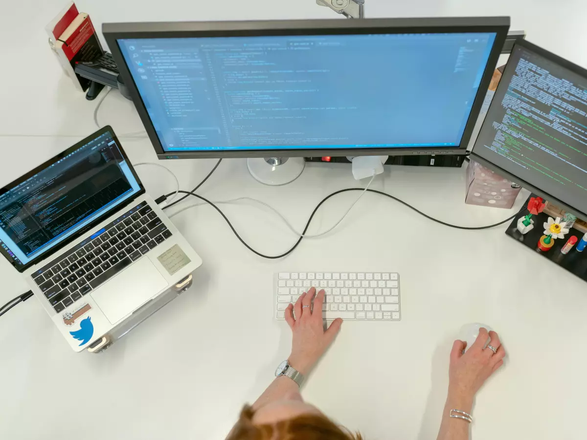 A person's hands typing on a keyboard in front of two computer monitors displaying code. The image captures the essence of code refactoring, a common activity for developers.