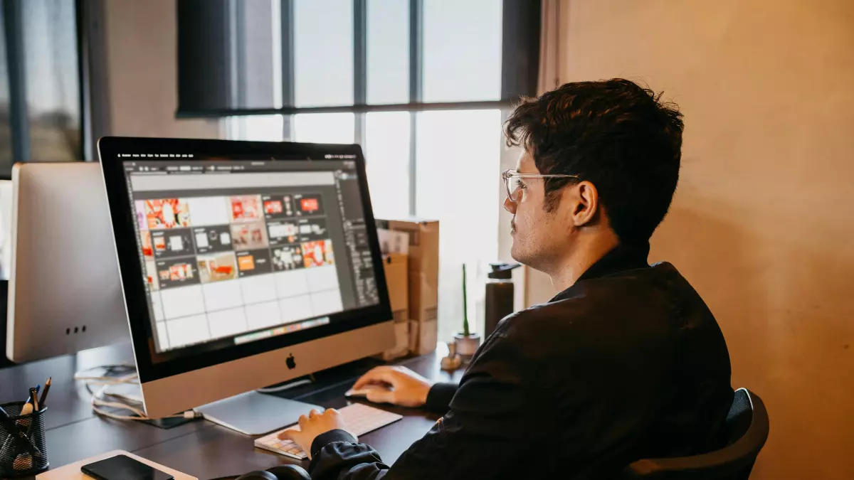 A man sits at a desk in front of a computer, typing on the keyboard.