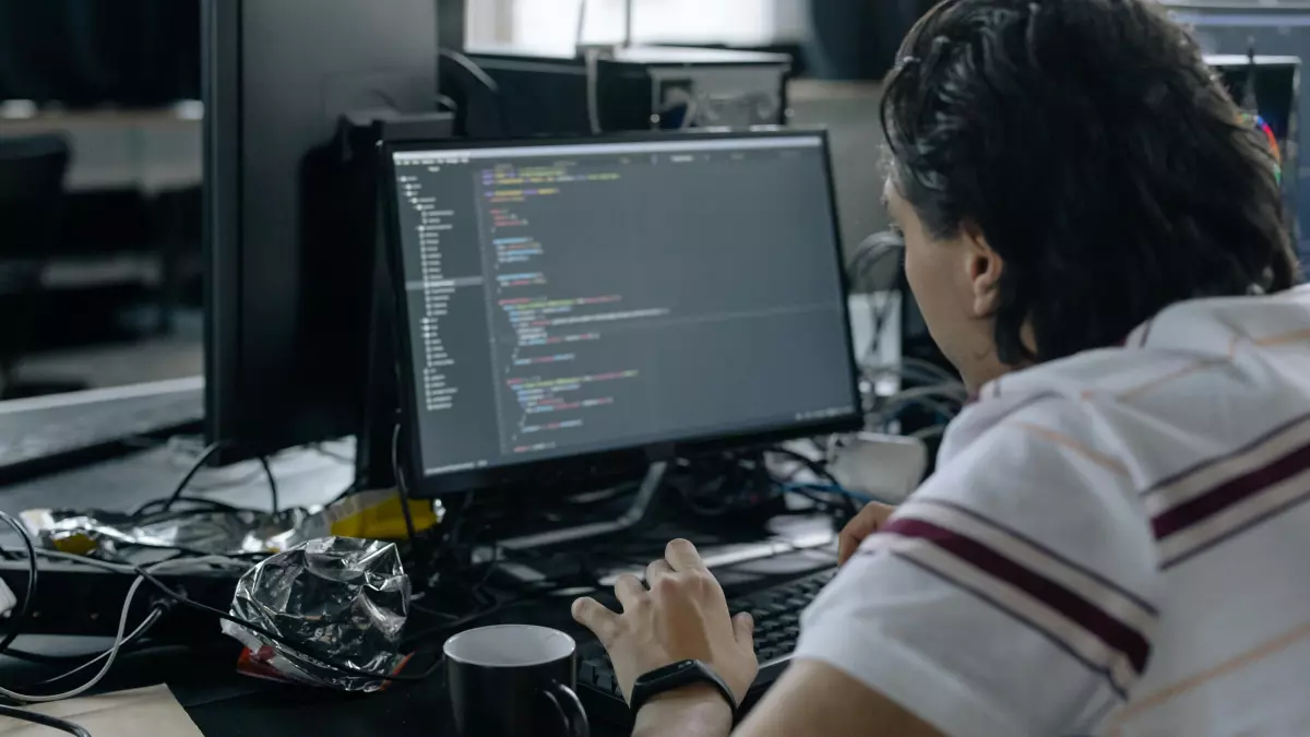 A person sitting at a desk, looking at a computer screen with code. The image suggests a serious and focused atmosphere