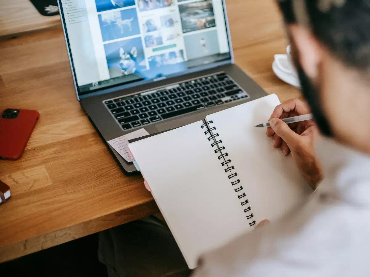 A person is working on a laptop, writing in a notebook.