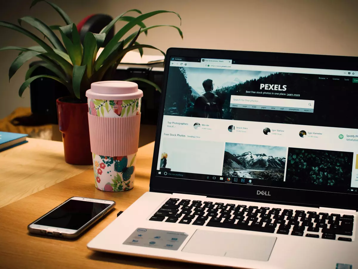 A laptop and a smartphone on a desk, with a coffee cup and a plant in the background