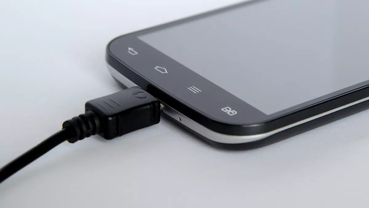 A close-up shot of a smartphone with a black charger cable plugged into it.