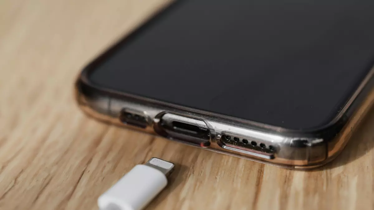 A white lightning cable connected to a phone and charging it.  The phone is on a wooden surface.