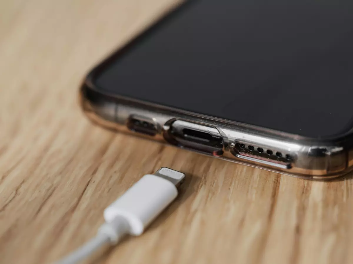 A white lightning cable connected to a phone and charging it.  The phone is on a wooden surface.