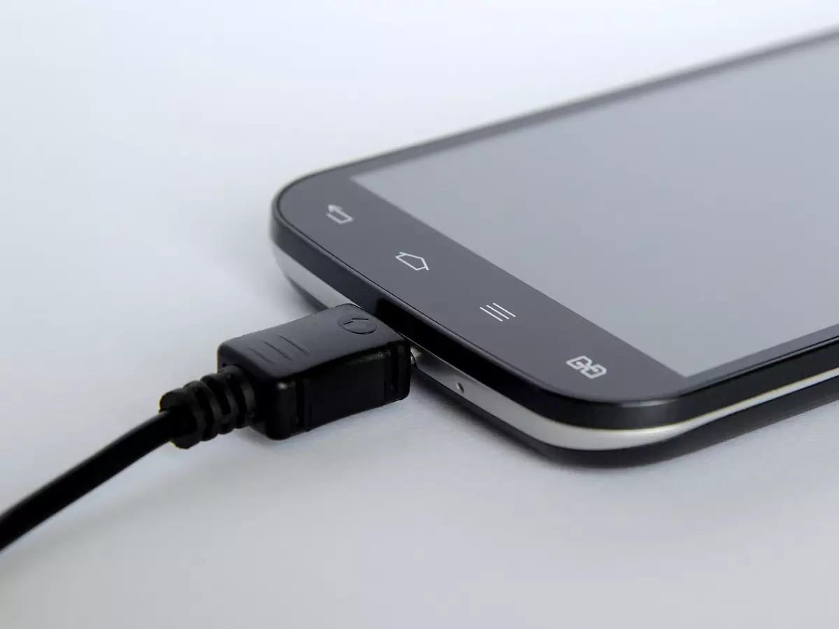 A close-up shot of a smartphone with a black charger cable plugged into it.