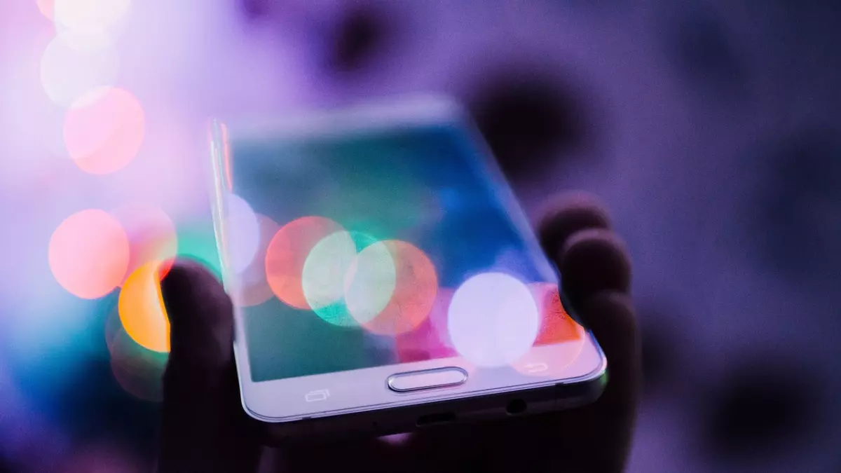 A close-up of a hand holding a smartphone with a blurred background of colorful lights.