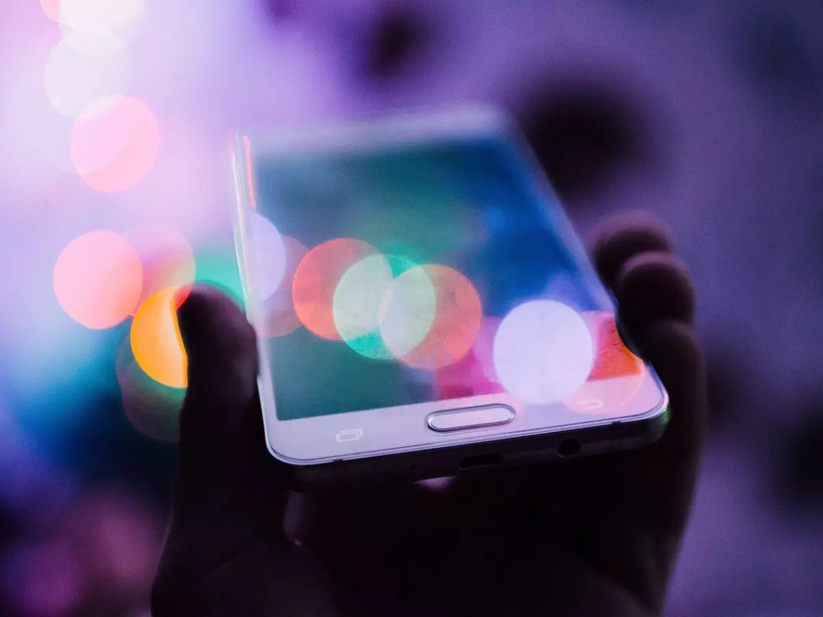 A close-up of a hand holding a smartphone with a blurred background of colorful lights.