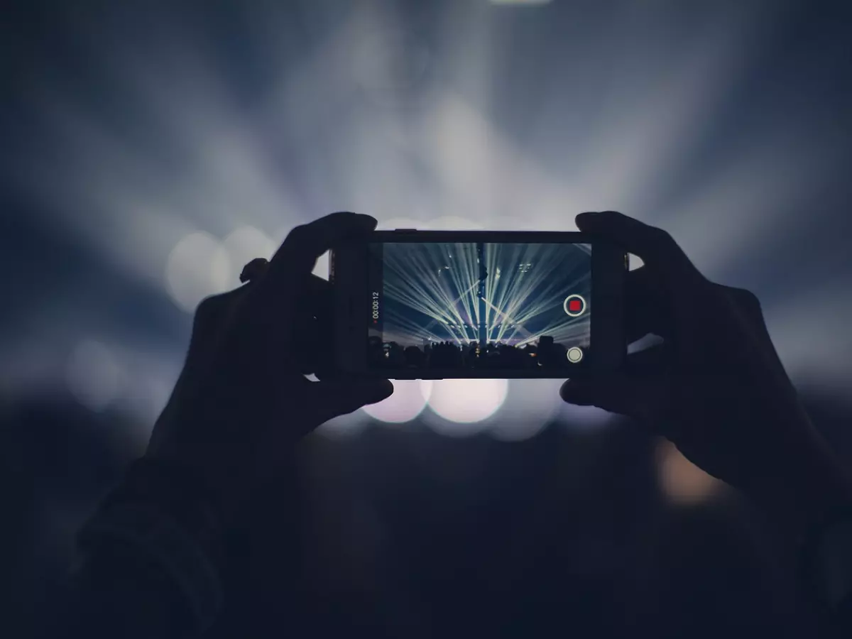 A smartphone captures the stage at a concert with complex lighting and crowd movement.