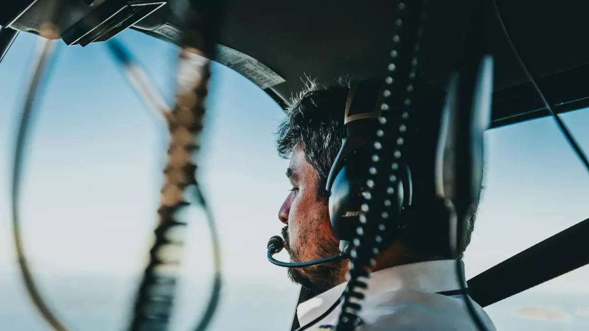 A close-up shot of a pilot in a cockpit, looking out the window, wearing headphones and a microphone. The image is focused on the pilot