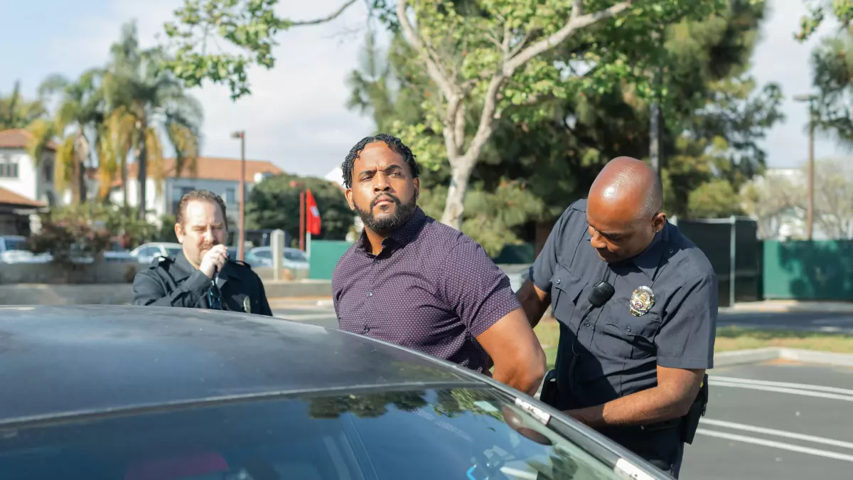 A man in handcuffs is being escorted by two police officers, one of whom is putting handcuffs on him.