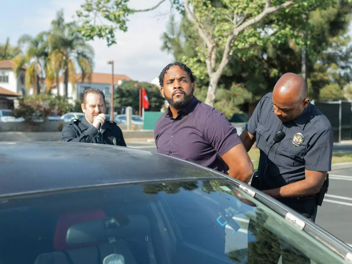 A man in handcuffs is being escorted by two police officers, one of whom is putting handcuffs on him.