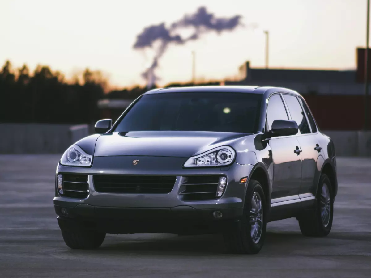 A silver Porsche Cayenne SUV parked in a parking lot at sunset.