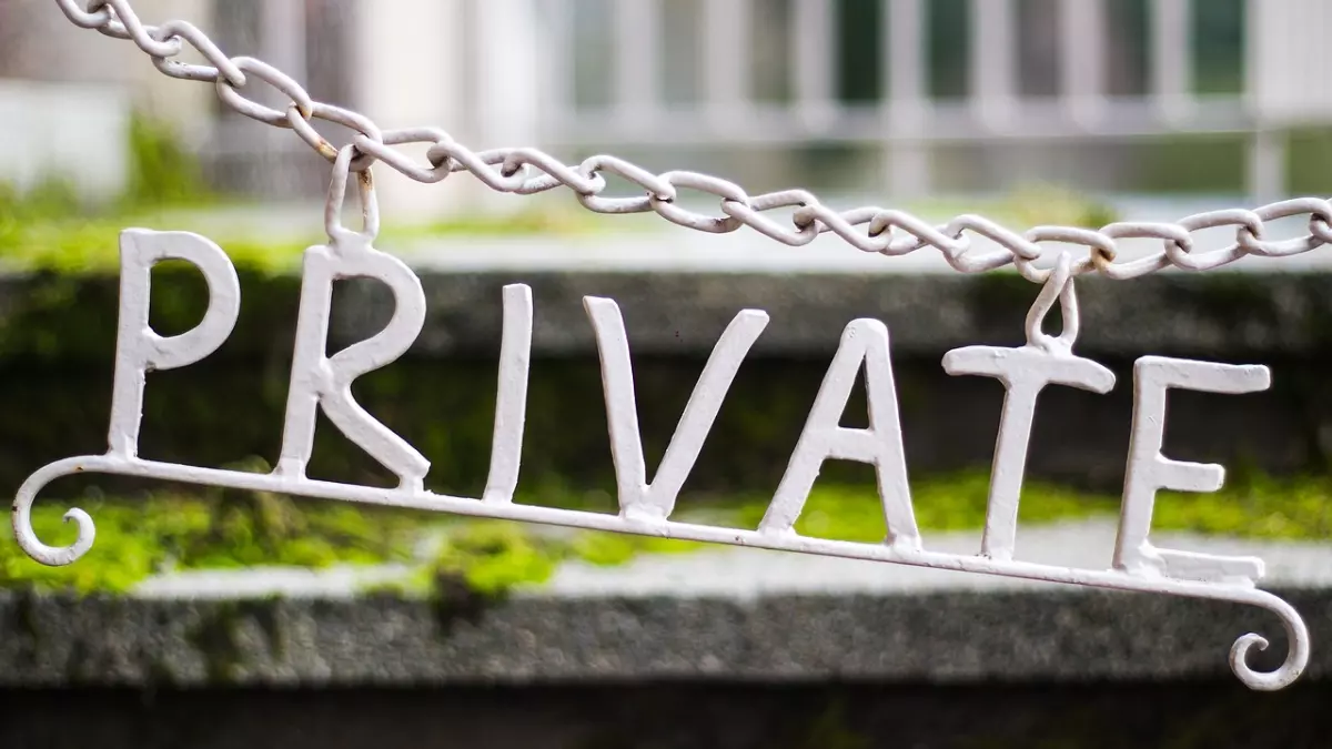 A white metal sign with the word "PRIVATE" hanging from a chain, with a blurred background.