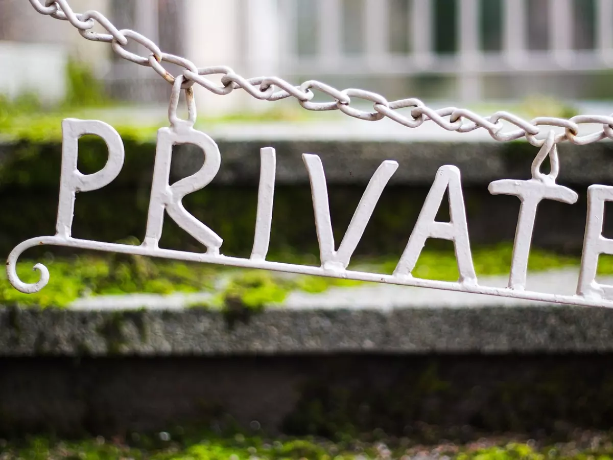 A white metal sign with the word "PRIVATE" hanging from a chain, with a blurred background.